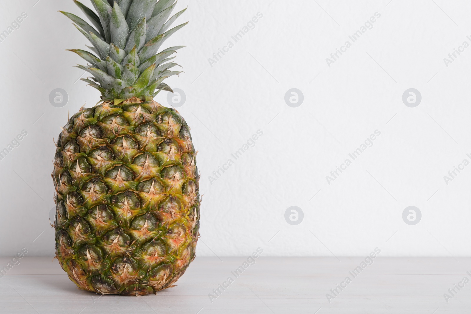 Photo of Whole ripe pineapple on white wooden table. Space for text