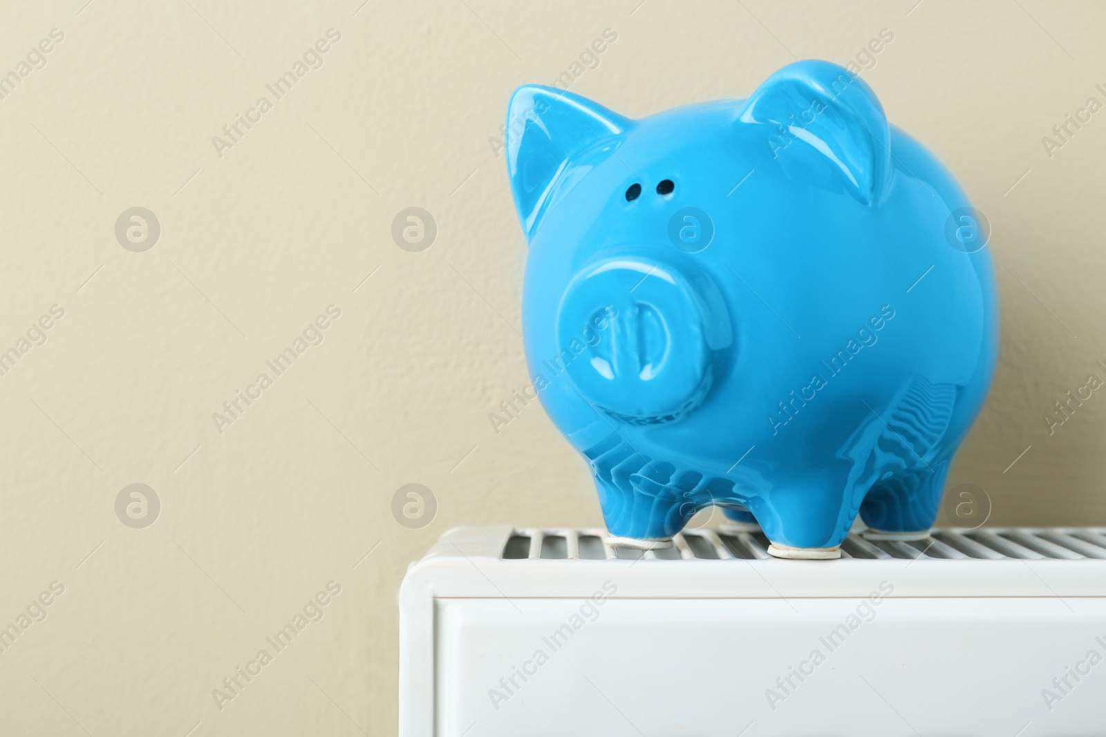 Photo of Piggy bank on heating radiator against beige background, space for text