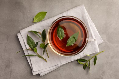Photo of Cup of freshly brewed tea with bay leaves on grey table, flat lay