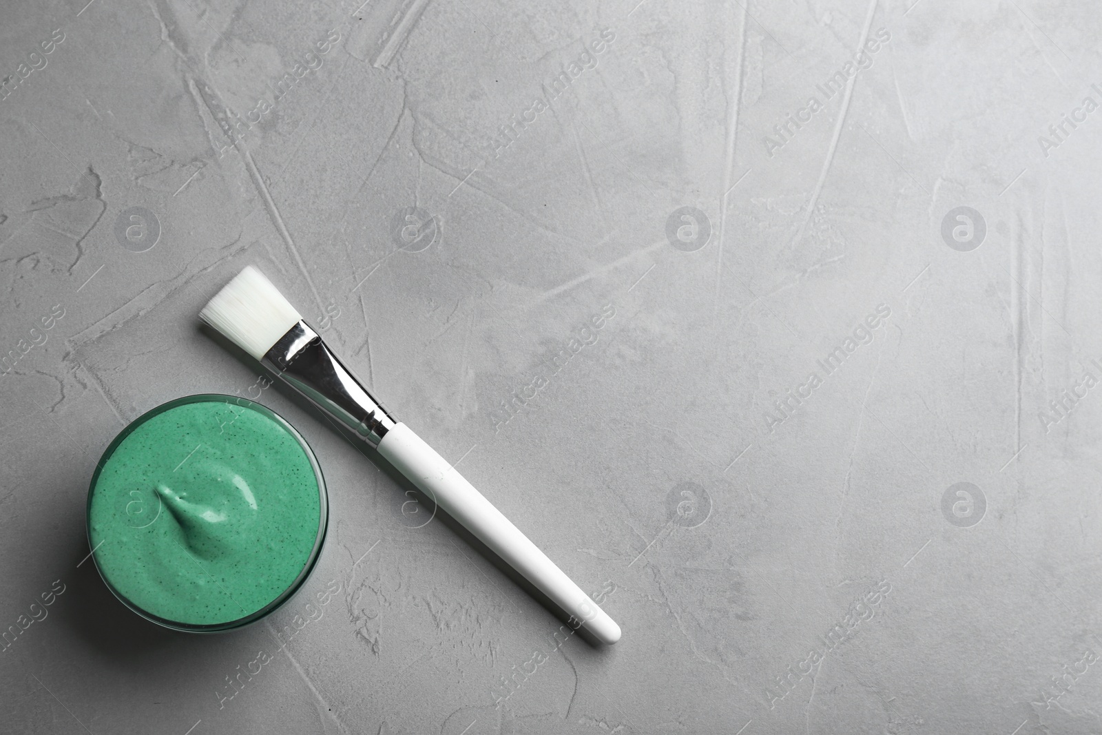 Photo of Freshly made spirulina facial mask in bowl and brush on light grey background, flat lay. Space for text