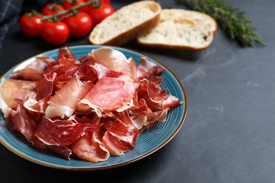 Photo of Tasty fresh prosciutto slices on black table