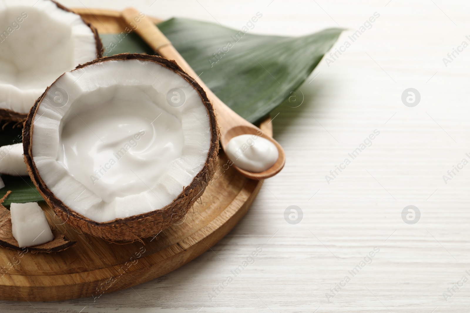 Photo of Ripe coconut and cream on white wooden table. Space for text