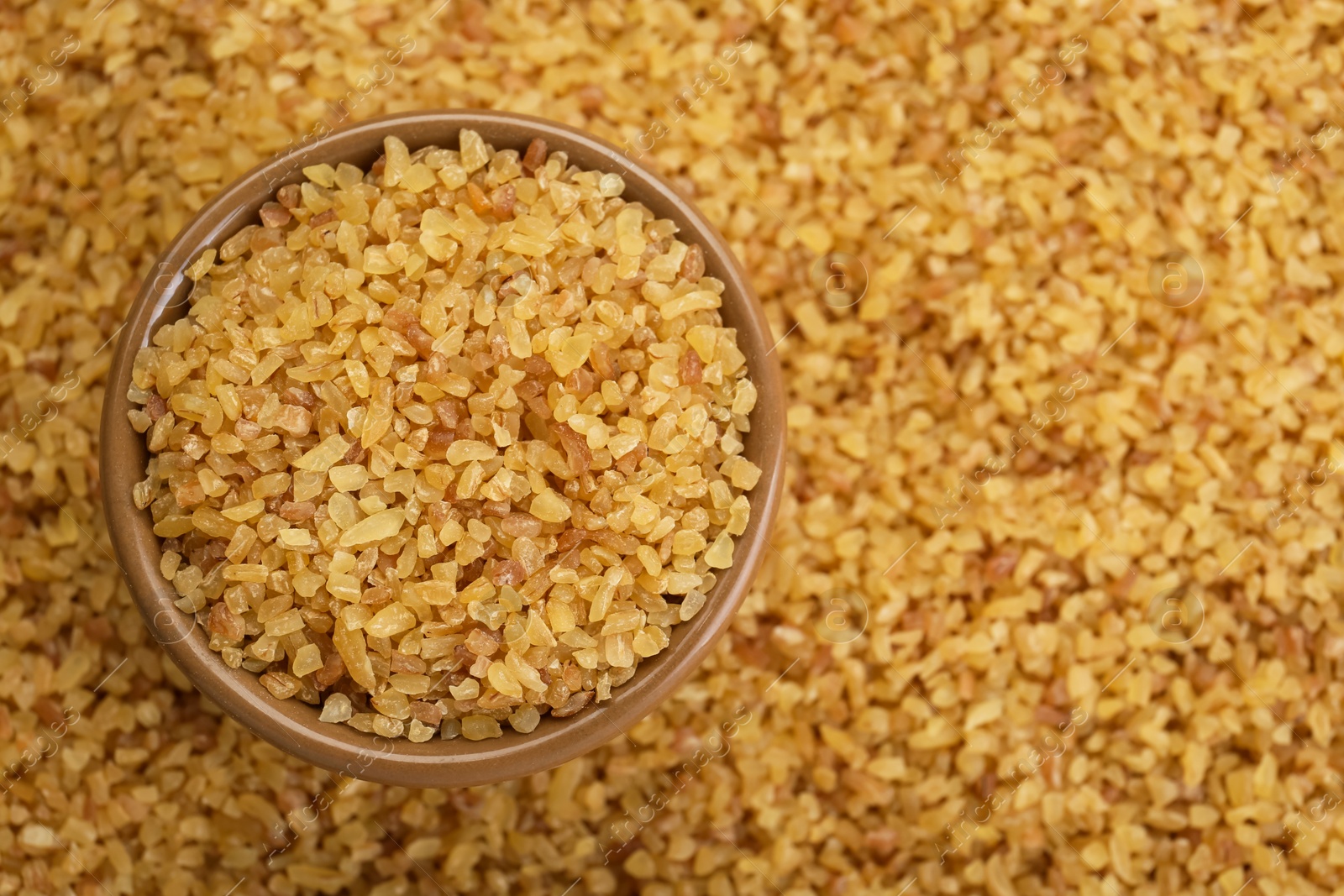 Photo of Bowl on pile of uncooked bulgur, top view. Space for text