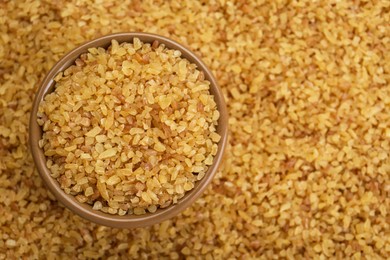 Photo of Bowl on pile of uncooked bulgur, top view. Space for text