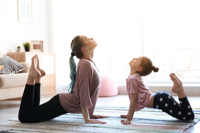Photo of Young mother and her daughter practicing yoga at home