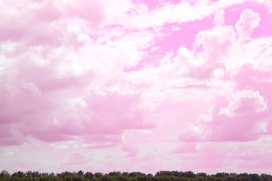 Image of Fantastic pink sky with fluffy clouds over green trees