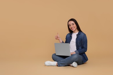Photo of Smiling young woman with laptop showing thumbs up on beige background, space for text