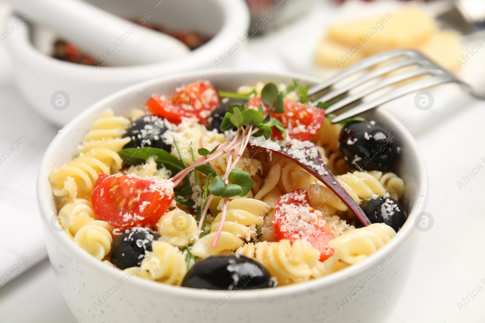 Photo of Bowl of delicious pasta with tomatoes, olives and cheese on white table, closeup