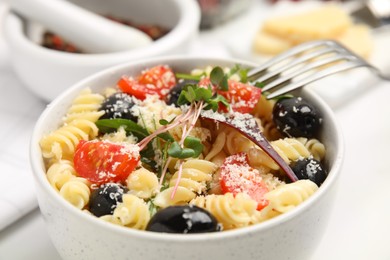 Photo of Bowl of delicious pasta with tomatoes, olives and cheese on white table, closeup