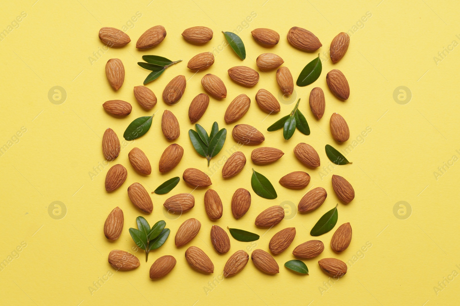 Photo of Delicious almonds and fresh leaves on yellow background, flat lay