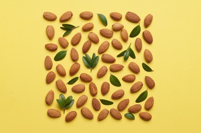 Photo of Delicious almonds and fresh leaves on yellow background, flat lay