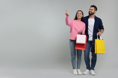 Happy couple with shopping bags looking at something on grey background. Space for text