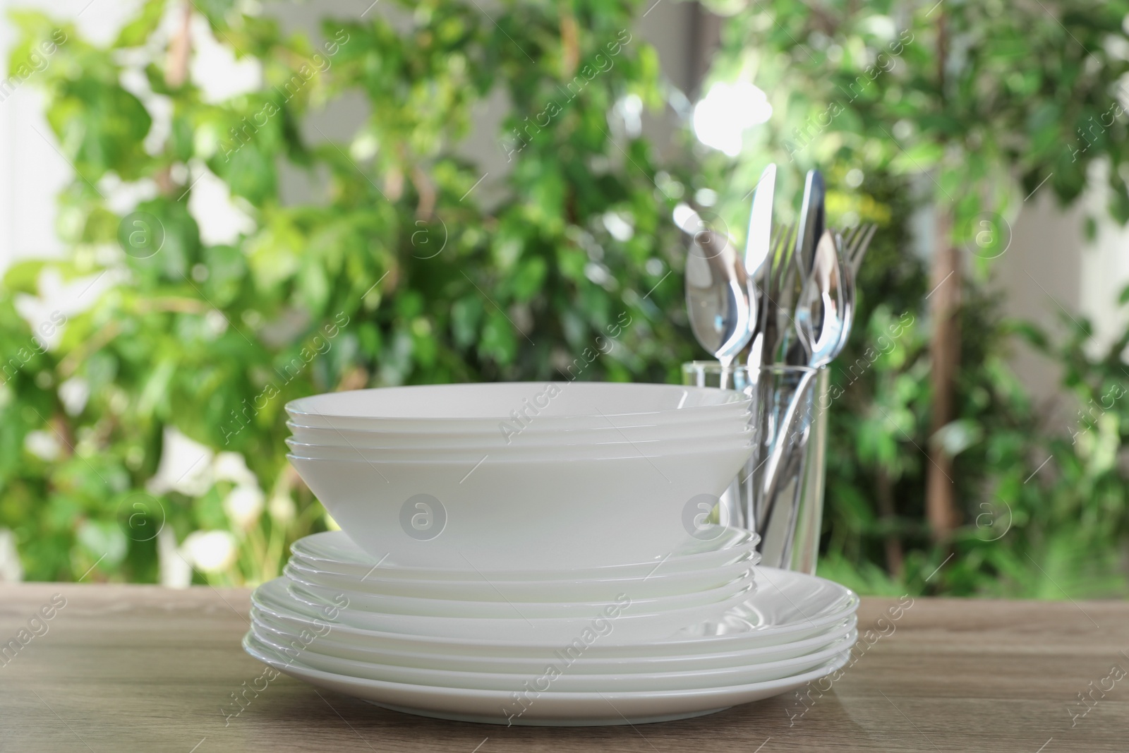 Photo of Clean dishes and glass with shiny cutlery on wooden table against blurred background