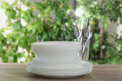 Clean dishes and glass with shiny cutlery on wooden table against blurred background