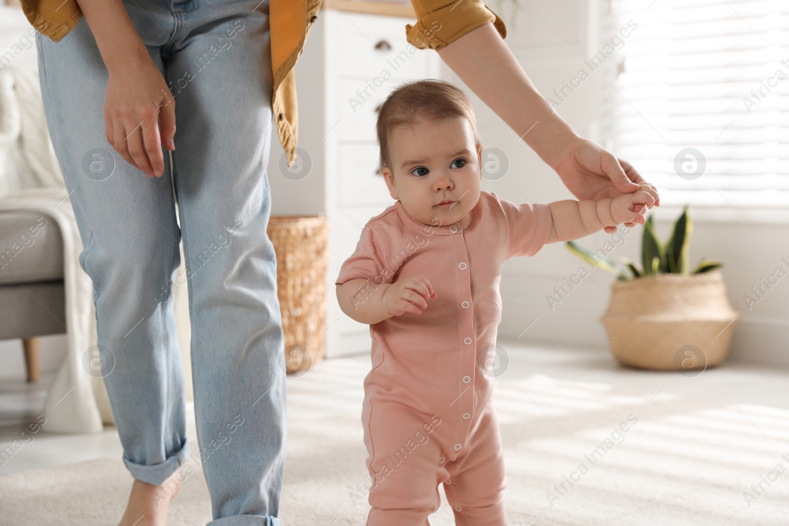 Photo of Mother supporting her baby daughter while she learning to walk at home