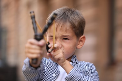 Photo of Little boy playing with slingshot outdoors on city street