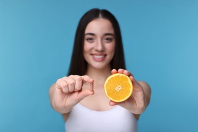 Photo of Beautiful young woman with vitamin pill and piece of orange on light blue background, selective focus