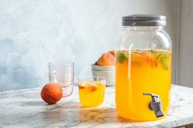 Photo of Peach cocktail in glass and jar with tap on table. Refreshing drink