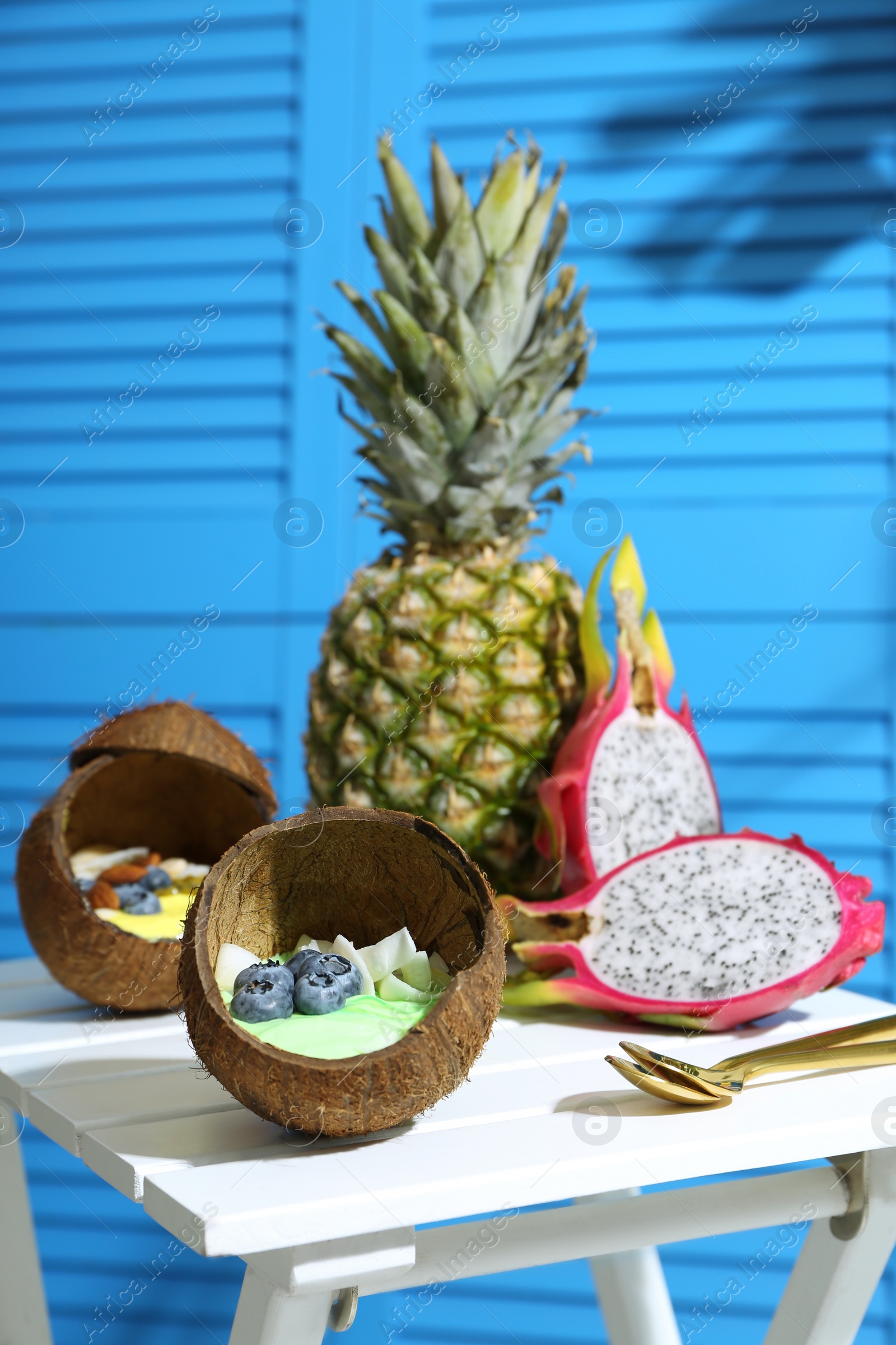 Photo of Tasty smoothie bowl served in coconut shells on white wooden table