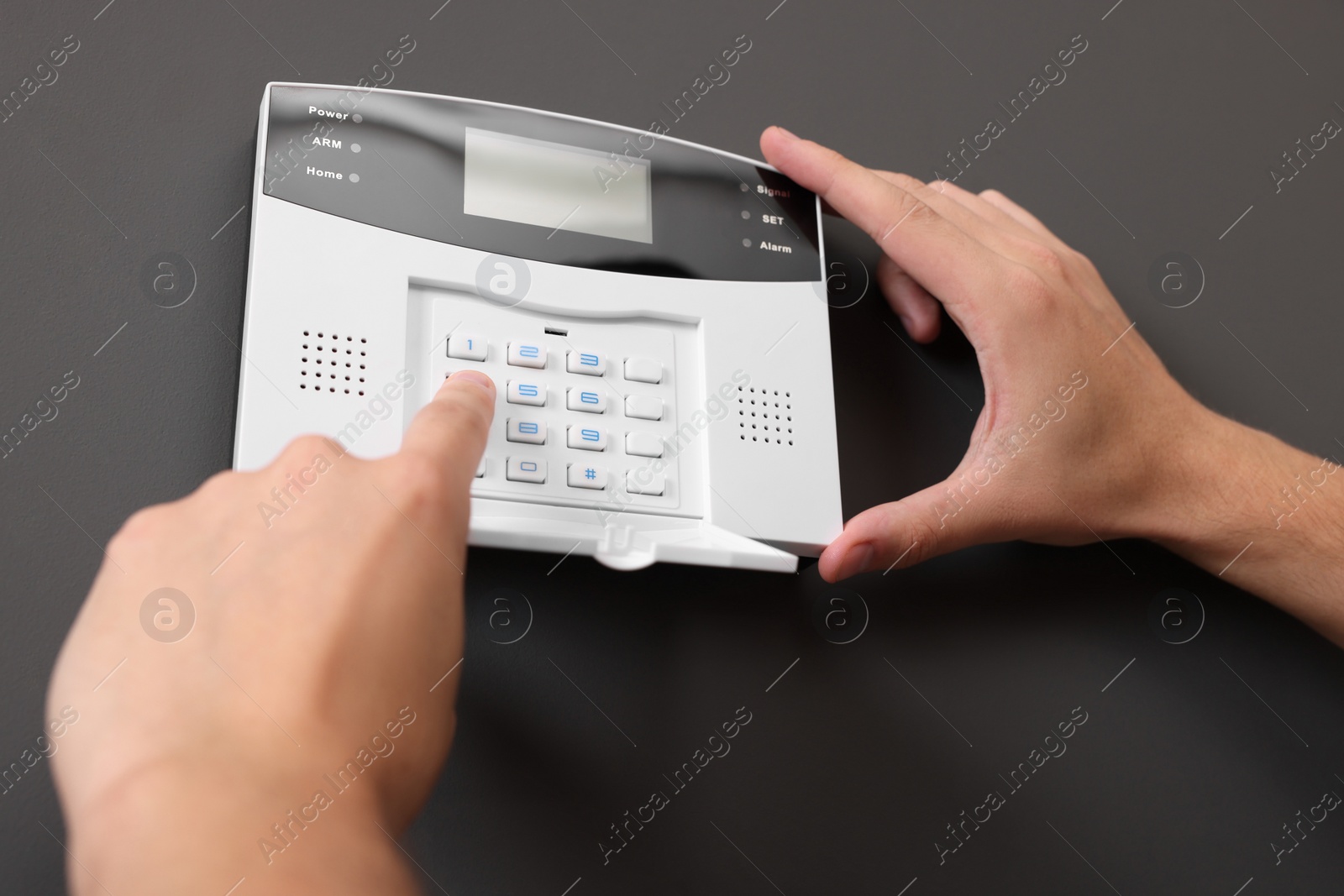 Photo of Man entering code on home security alarm system near gray wall, closeup