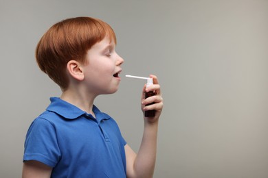 Photo of Little boy using throat spray on grey background