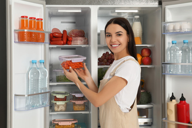 Photo of Young woman with lunchbox of carrots near refrigerator