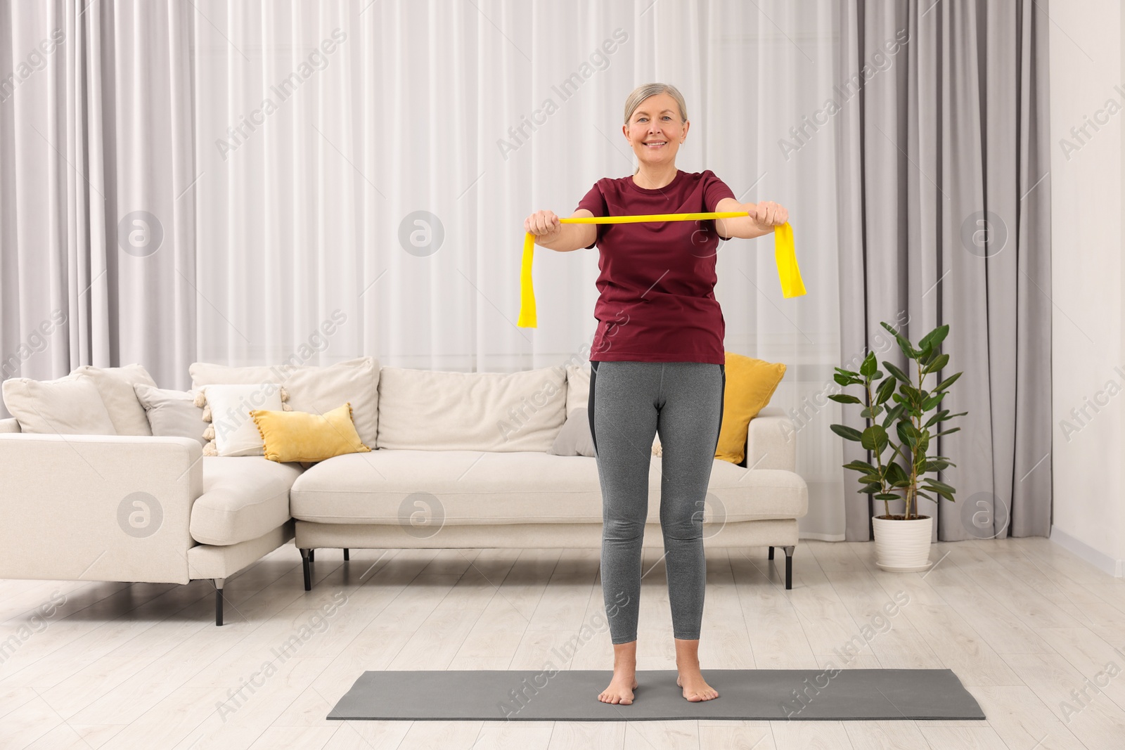 Photo of Senior woman doing exercise with fitness elastic band on mat at home