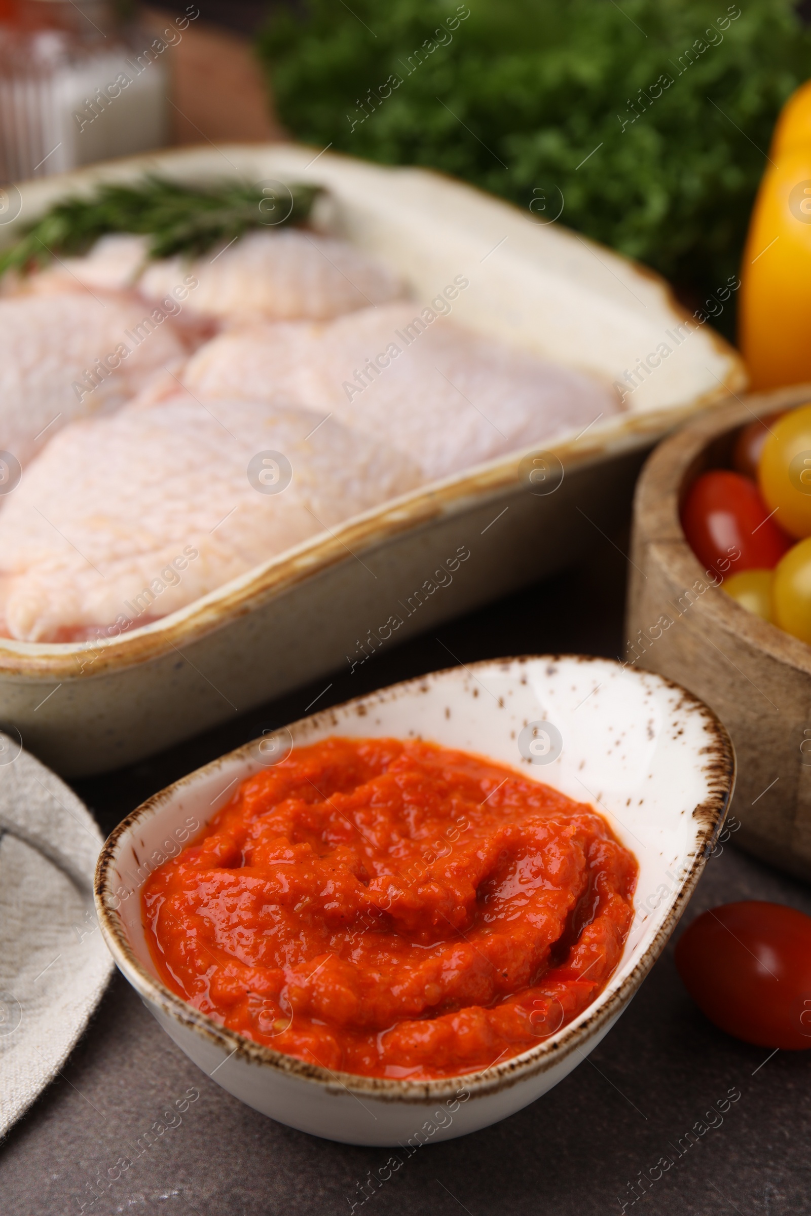 Photo of Fresh marinade, raw chicken and tomatoes on brown table, closeup