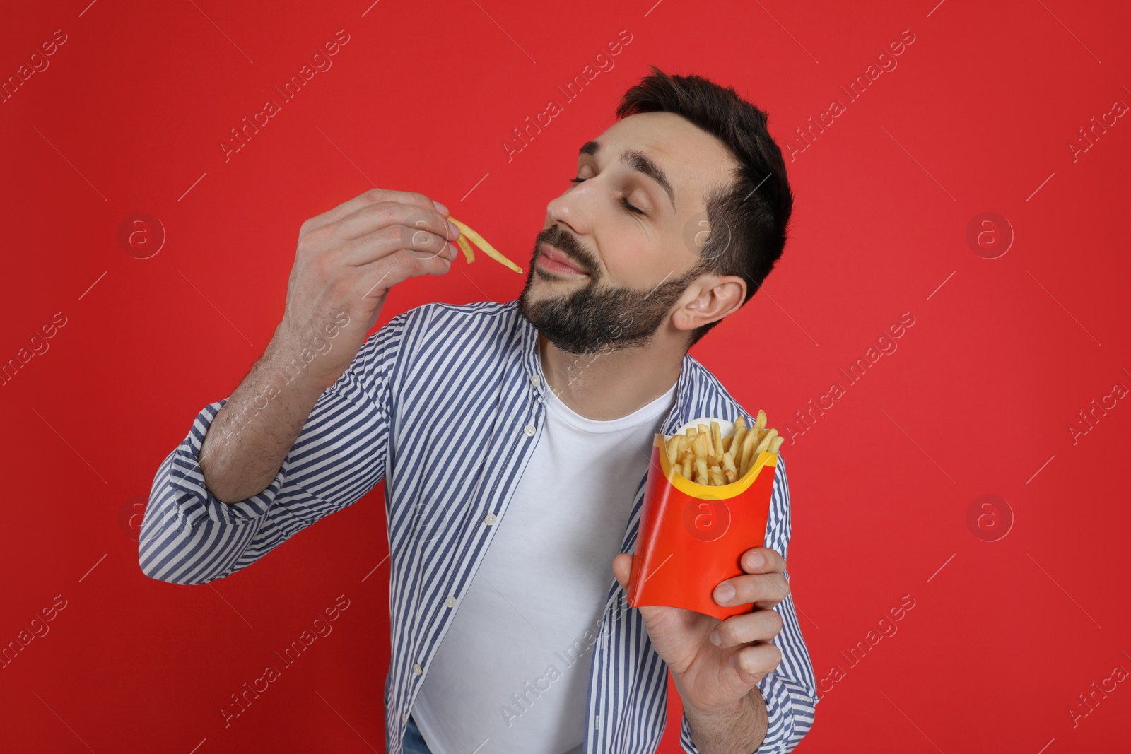 Photo of Man eating French fries on red background