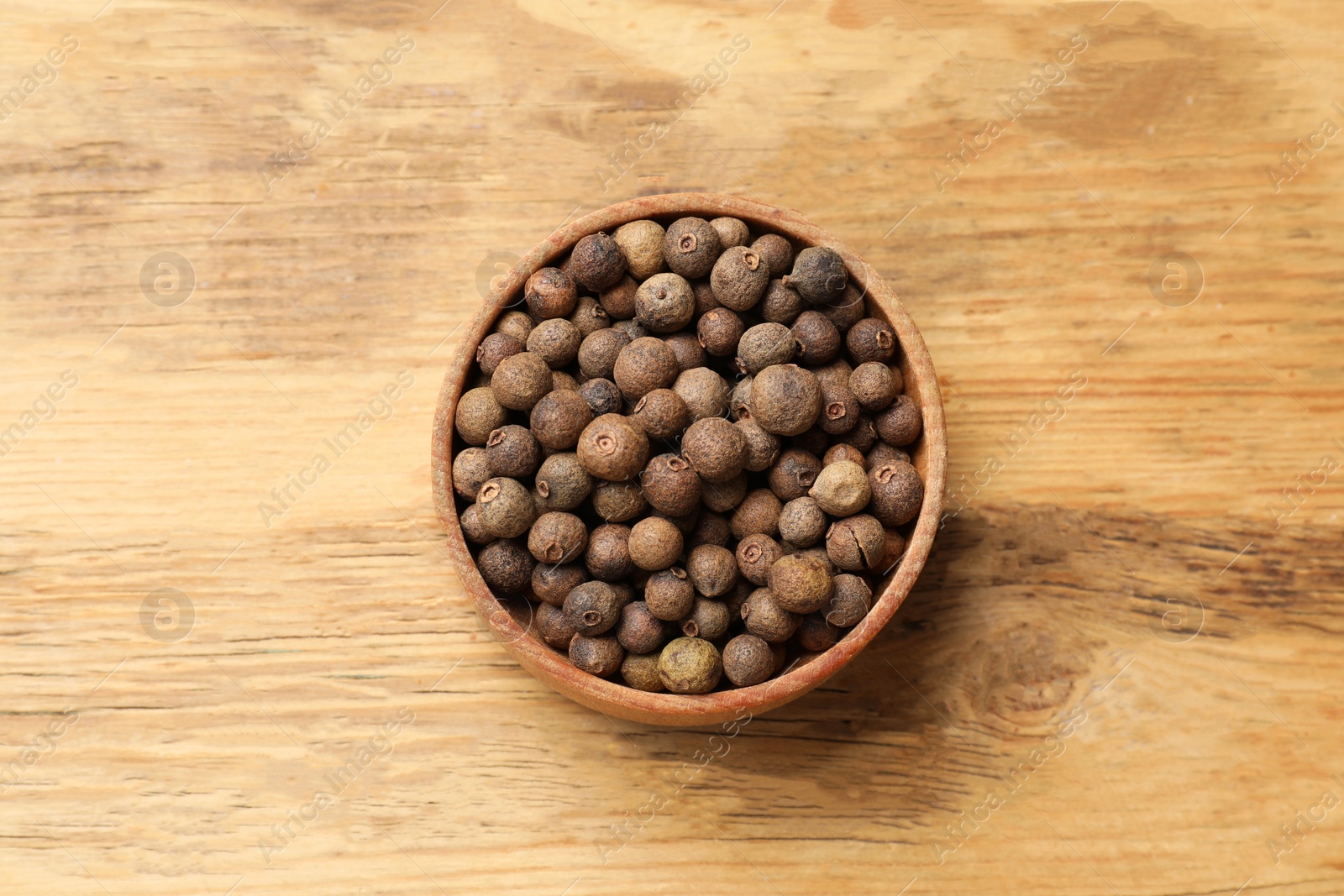 Photo of Dry allspice berries (Jamaica pepper) in bowl on wooden table, top view