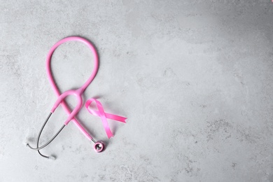 Photo of Pink ribbon and stethoscope on light background, top view with space for text. Breast cancer concept