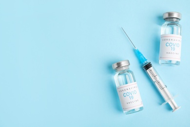 Photo of Vials with coronavirus vaccine and syringe on light blue background, flat lay. Space for text