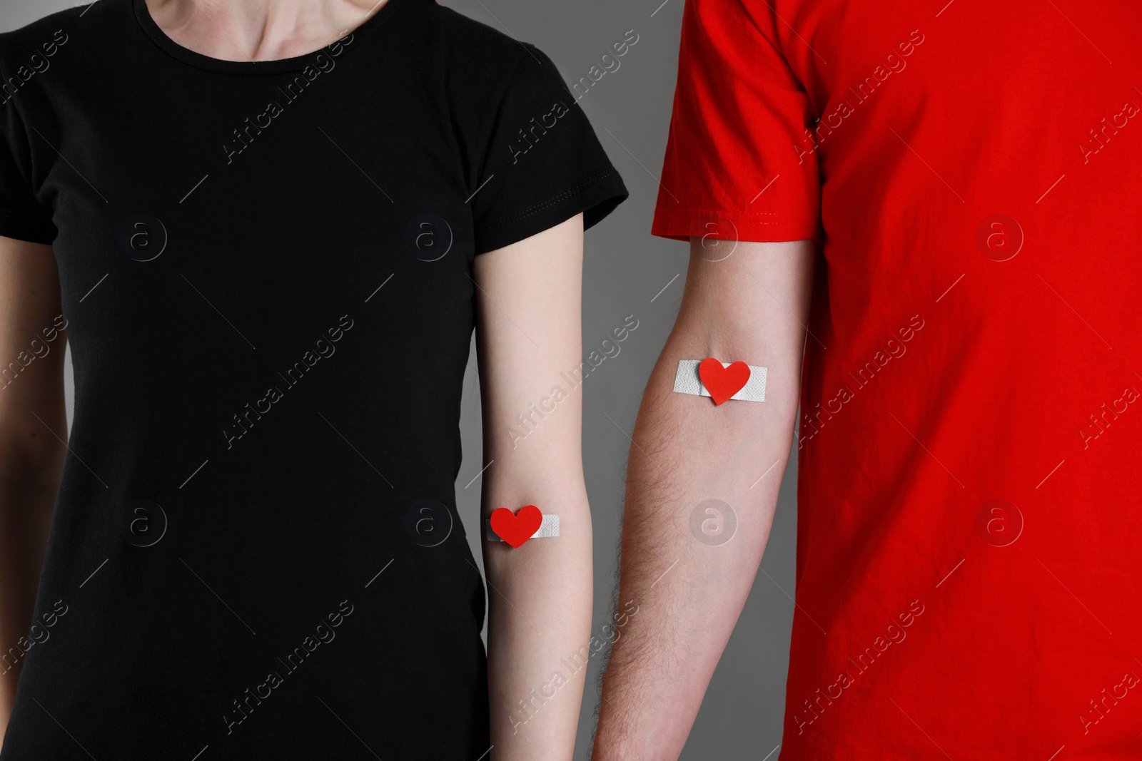 Photo of Blood donation concept. Couple with adhesive plasters on arms against grey background, closeup