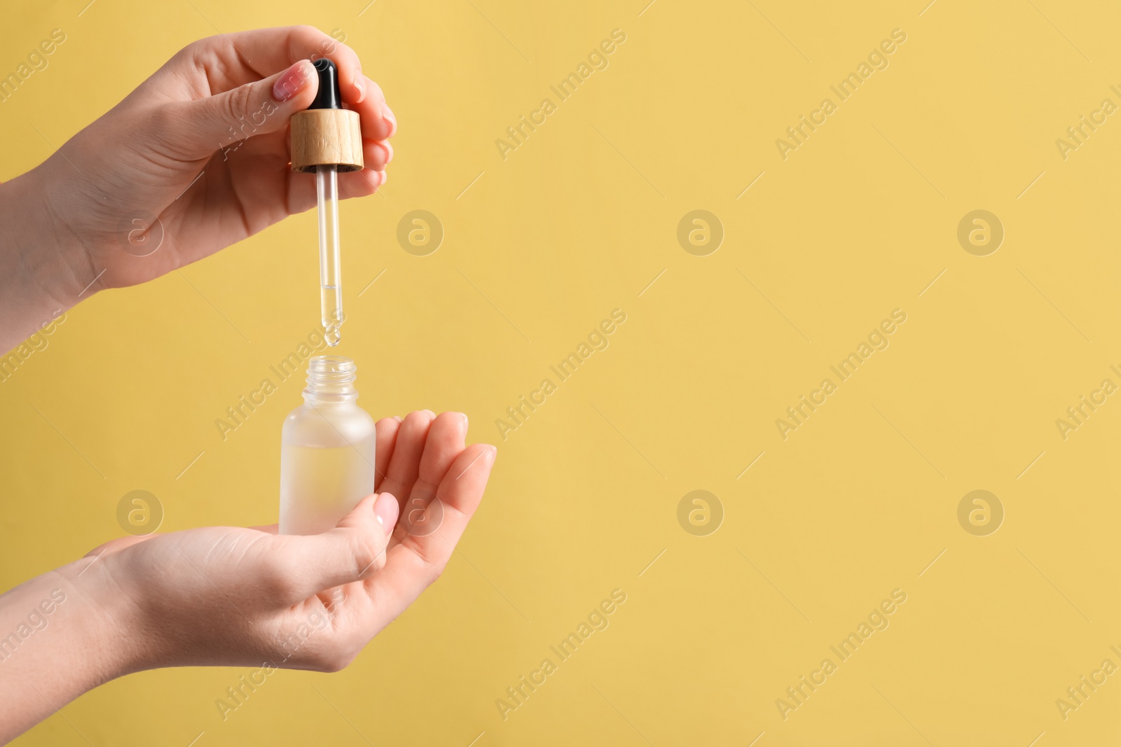 Photo of Woman dripping serum from pipette into bottle against pale orange background, closeup. Space for text