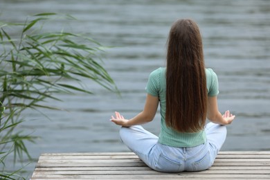 Teenage girl meditating near river, back view
