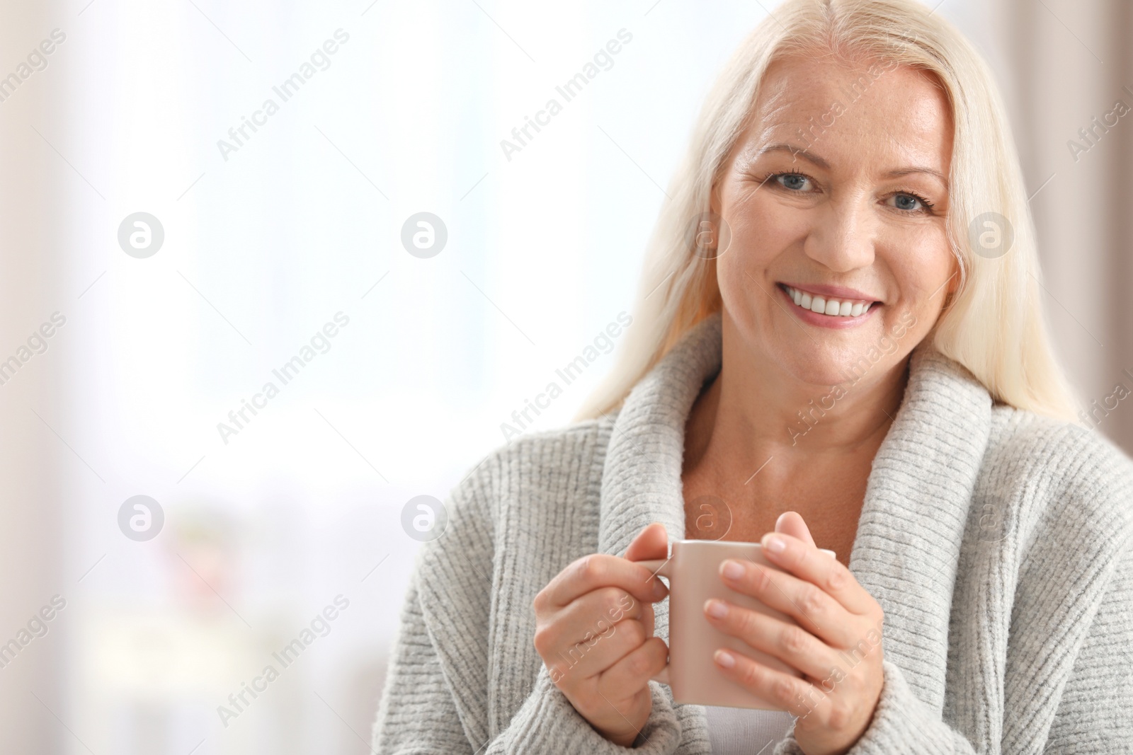 Photo of Portrait of beautiful older woman with cup of tea against blurred background. Space for text