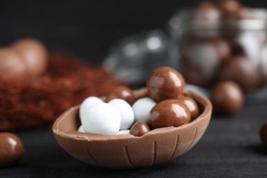 Half of tasty chocolate egg with candies on black wooden table, closeup. Space for text