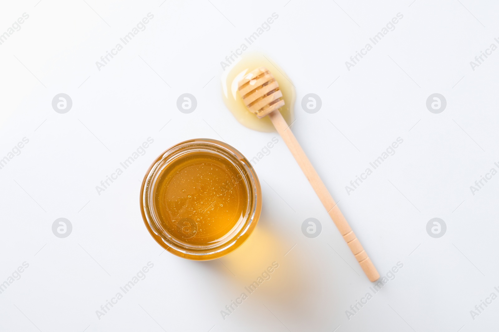 Photo of Tasty honey in glass jar and dipper on white background, top view