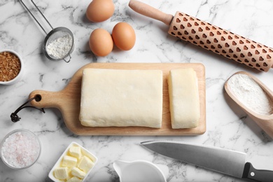 Flat lay composition of puff pastry dough and ingredients on white marble table