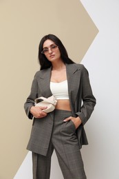Photo of Beautiful woman with sunglasses and bag in formal suit on color background. Business attire