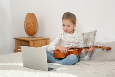 Photo of Little girl learning to play ukulele with online music course at home. Time for hobby