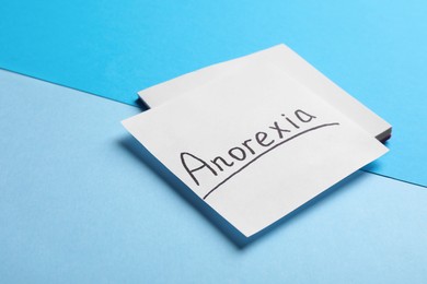 Photo of Note papers with word Anorexia on light blue background, closeup