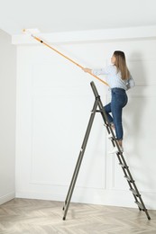 Photo of Young woman painting ceiling with white dye indoors