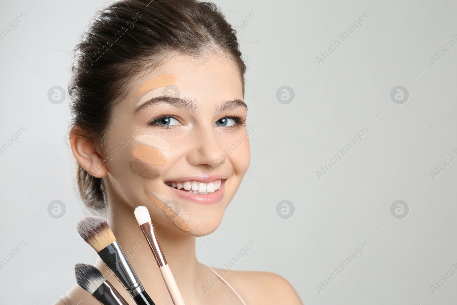 Photo of Beautiful girl on light grey background. Using concealers and foundation for face contouring