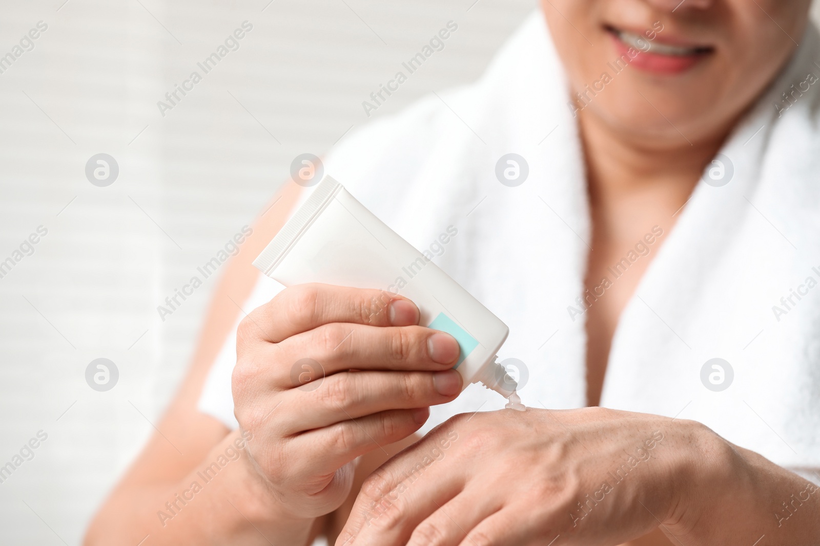 Photo of Man applying body cream onto his hand indoors, closeup
