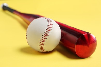Photo of Baseball bat and ball on yellow background, closeup