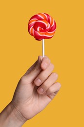 Photo of Woman holding bright tasty lollipop on orange background, closeup