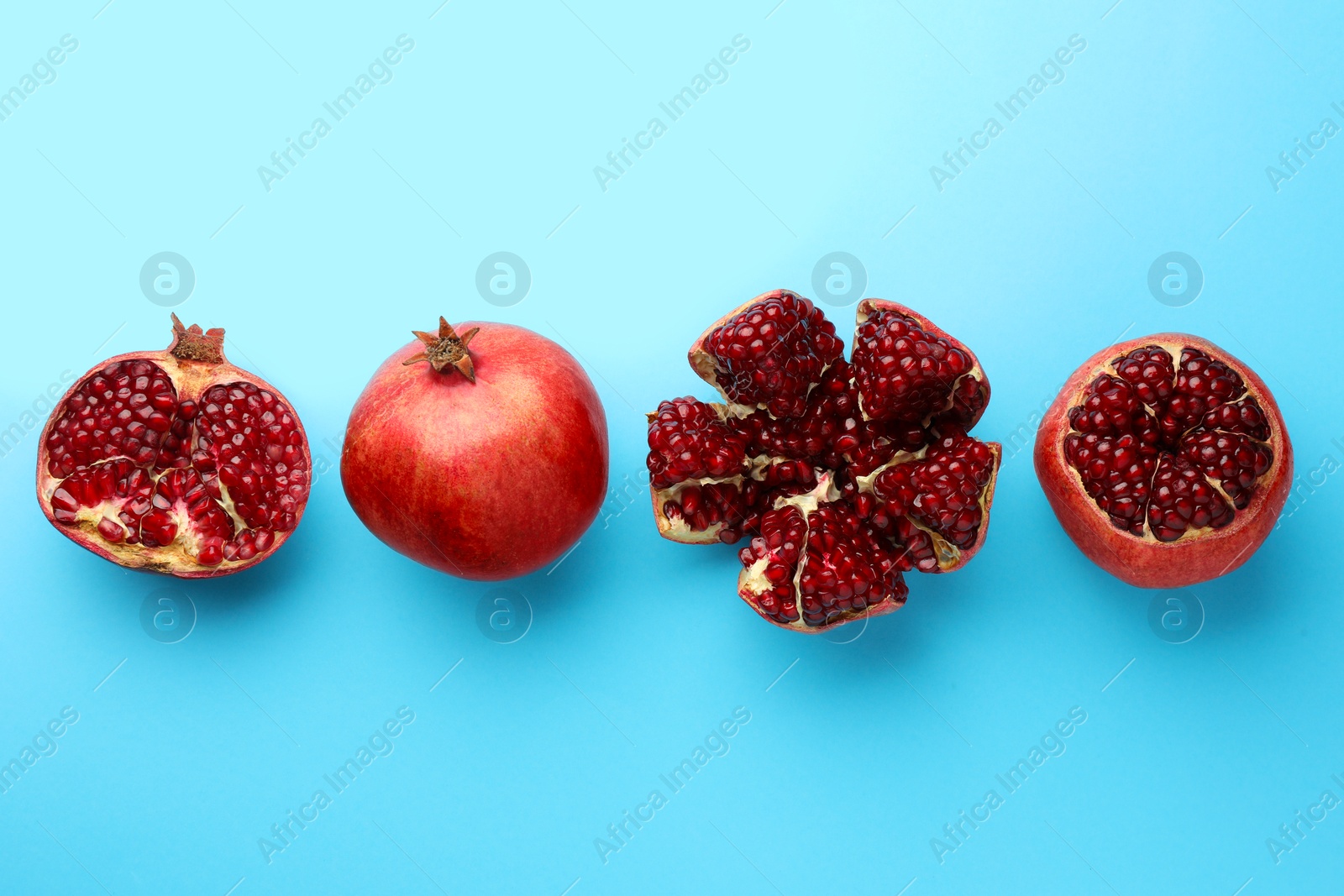 Photo of Whole and cut fresh pomegranates on light blue background, flat lay