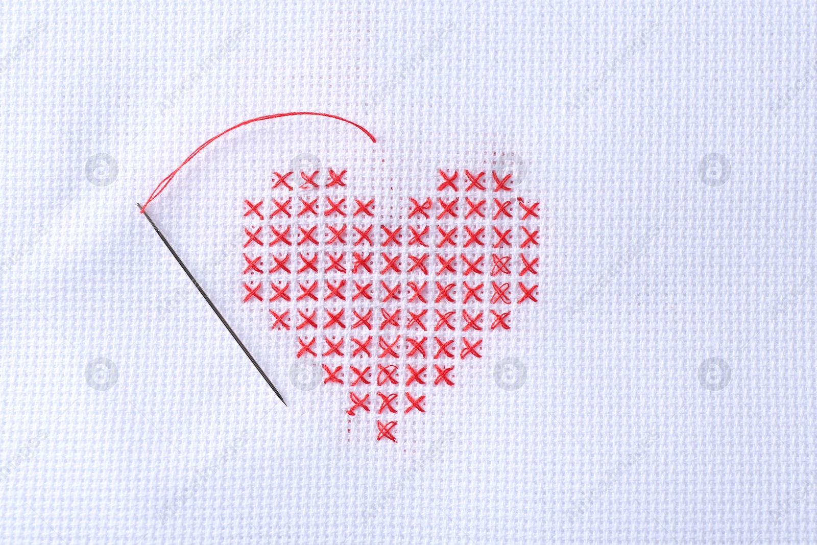 Photo of Embroidered red heart and needle on white cloth, top view