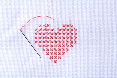 Embroidered red heart and needle on white cloth, top view